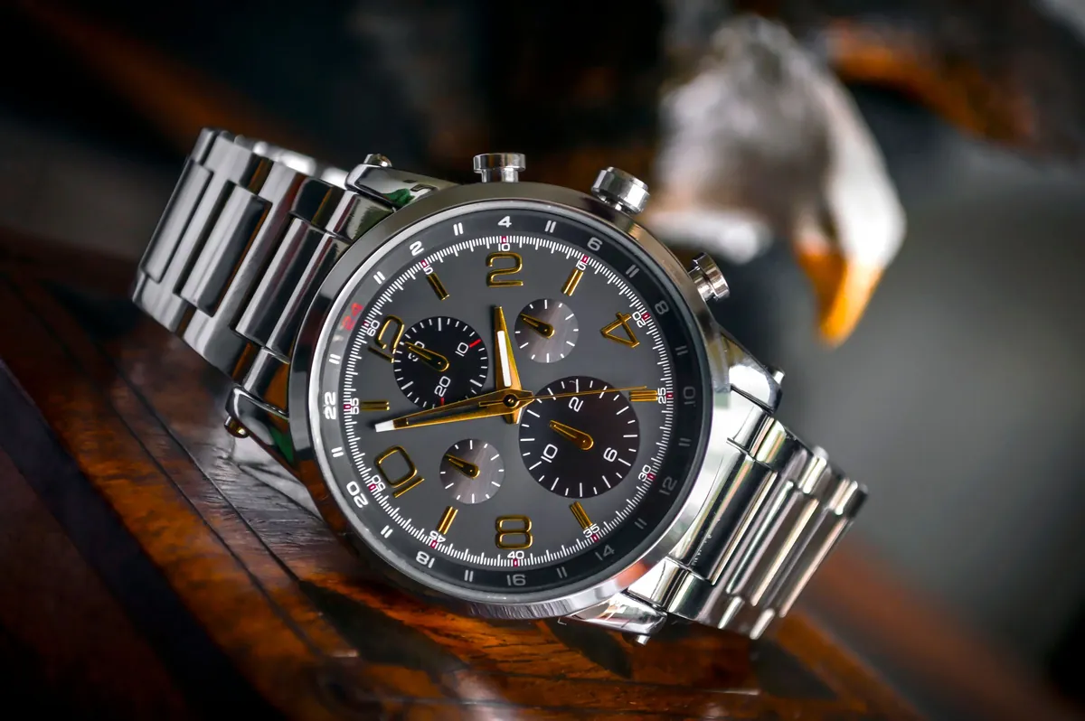 Montre chronographe en acier à cadran gris et aiguilles dorées, bracelet métal, sur un bois sombre