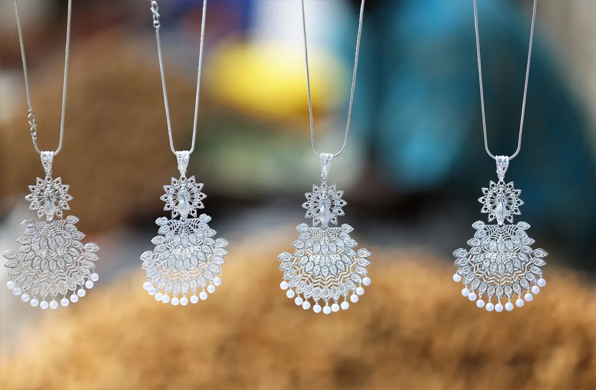 Quatre pendentifs en métal argenté ouvragé, avec perles et pampilles, suspendus à des chaînes fines