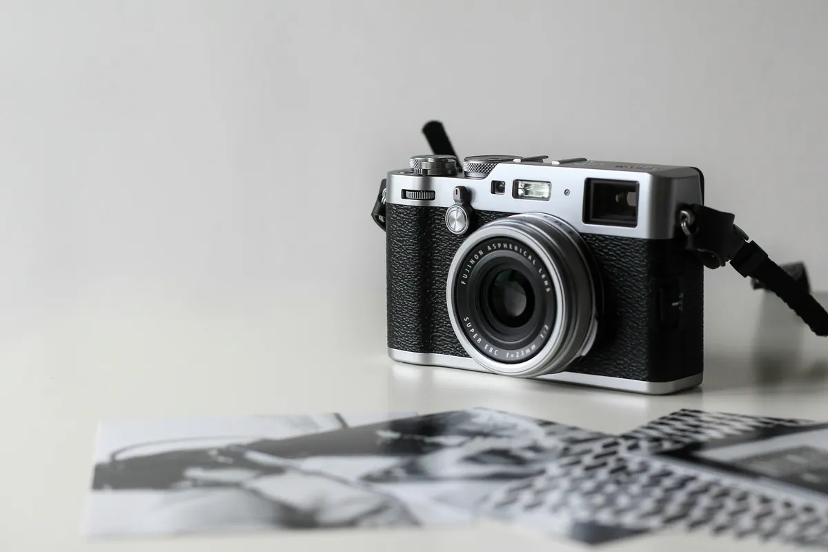 Appareil photo compact argenté et noir au style rétro, avec sa dragonne, sur des tirages en noir et blanc