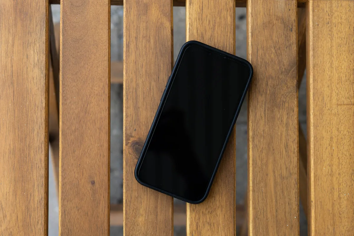 Smartphone noir écran éteint, posé à plat sur des lattes de bois, vu du dessus