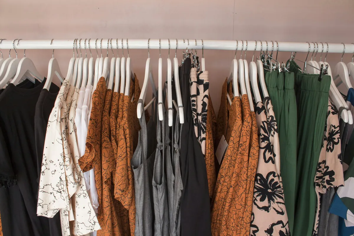 Portant de vêtements pour femme sur cintres blancs : chemisiers à motifs, robe imprimée et pantalon vert