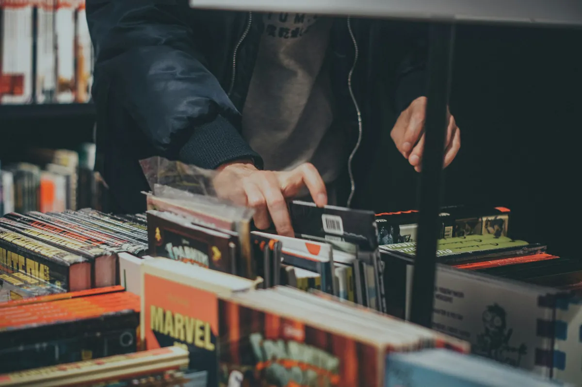 Mains qui feuillettent des bacs de vinyles et de bandes dessinées chez un disquaire