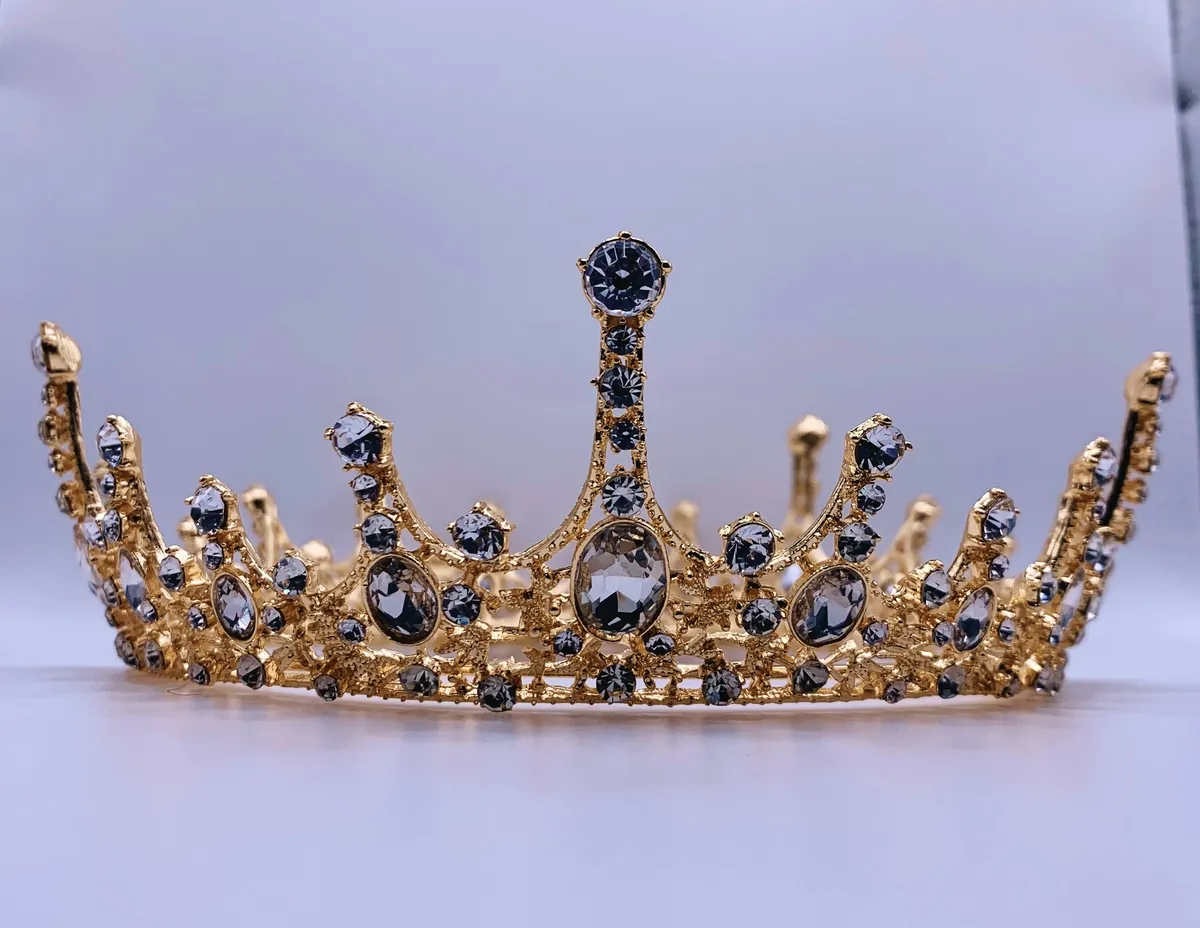 Diadème doré serti de pierres sombres et de strass sur fond mauve clair