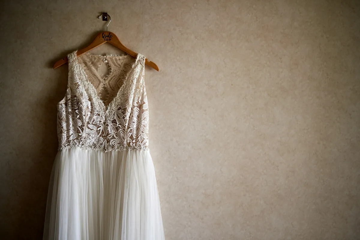 Robe de mariée blanche à bustier en dentelle et jupe en tulle, suspendue à un cintre contre un mur beige