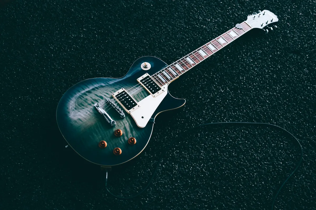 Guitare électrique à corps vert foncé posée à plat sur une surface sombre, câble branché