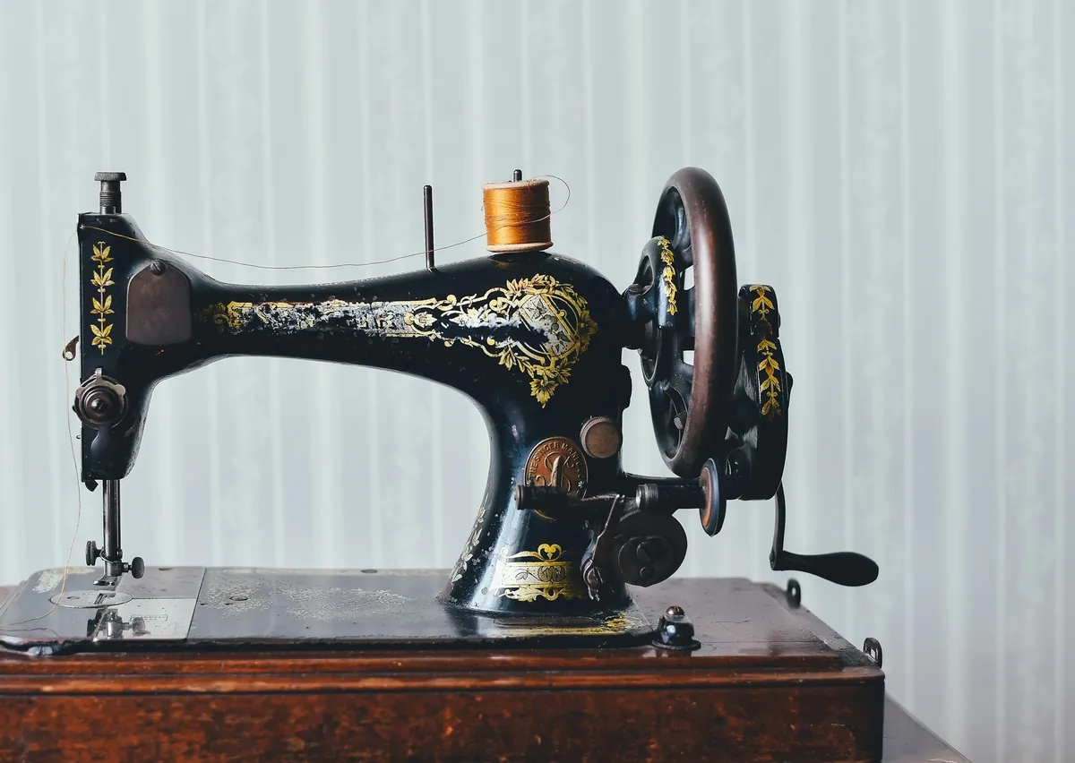Machine à coudre ancienne noire à décor doré et volant manuel, sur un meuble en bois