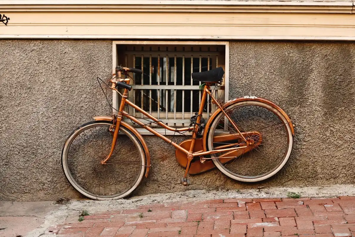 Vélo de ville ancien couleur cuivre appuyé contre un mur crépi, sous une fenêtre à barreaux